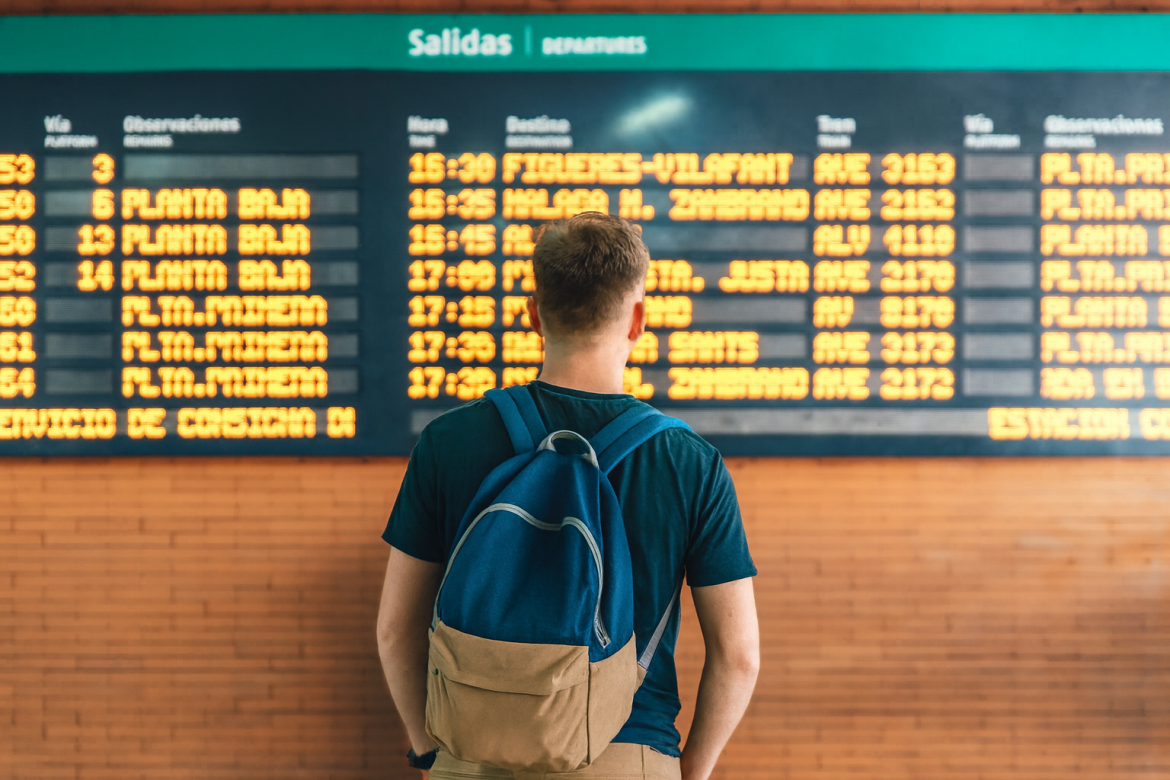 Viajero en estación de tren consultando el panel de salidas tras cancelación de trenes por incendios